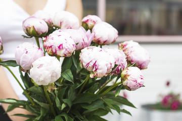 Young female florist holding bouquet of white pink peonies in street at flower shop