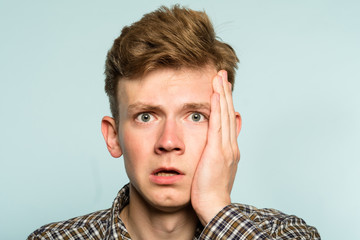 scared shocked terrified frightened startled man clutching hands to his face. portrait of a young guy on light background. emotion facial expression. feelings and people reaction concept.