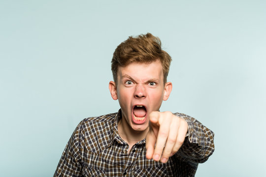 angry mental man screaming and pointing a finger. crazy infuriated berserk person. portrait of a young guy on light background. emotion facial expression. feelings and people reaction.