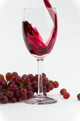 Red wine poured into a wine glass with fresh grapes. Isolated photo.