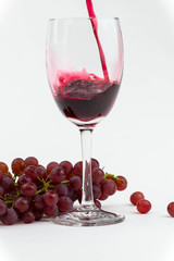 Red wine poured into a wine glass with fresh grapes. Isolated photo.