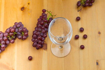 Obraz na płótnie Canvas Empty wine glass on a wooden table with fresh grapes scattered around