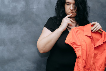Overweight, low self-esteem, body shaming. Obese shy woman hesitating to wear vibrant colored shirt