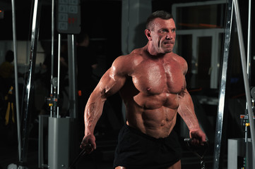 Close-up - Strong muscular bodybuilder working out on simulator machine . Male fitness model with naked torso posing in gym