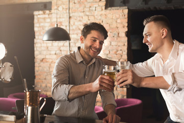 Two happy young men talking and drinking beer at bar
