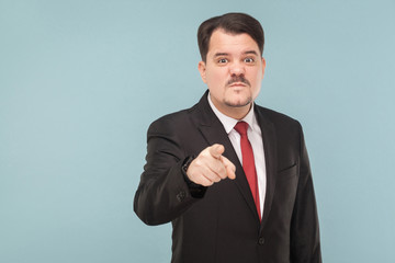 Boss have bad mood. I warn you the last time, I'm seriously! indoor studio shot. isolated on blue background. handsome businessman with black suit, red tie and mustache pointing and looking at camera