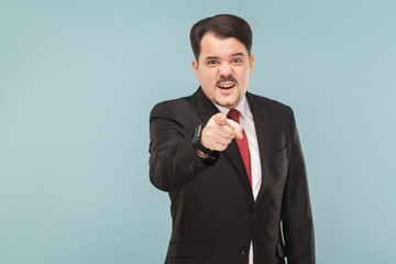 Hey you! Man in suit looking at pointing finger at camera. It's you? I do not believe you lie. indoor studio shot. isolated on blue background. businessman with black suit, red tie and mustache