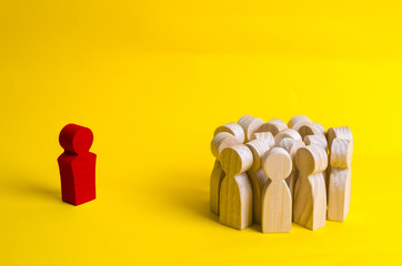 The crowd of wooden figures of people stand distantly and look at the red man. The rejected person...