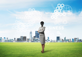 Camera headed woman standing on green grass against modern cityscape