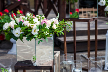 bouquets of flowers standing in unusual mirrored square vases. decorations are situated on the wooden stands outdoor