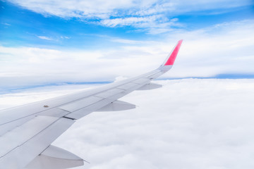 Obraz premium Wing of airplane flying above the clouds blue sky background. View form the window plane through.