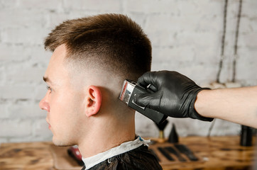 Barber does hair cut young guy on a brick wall background.