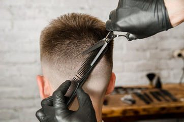 Barber does hair cut of nape young guy on a brick wall background. Back view.