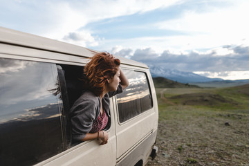 young ginger girl watching from the window of the van on beautiful mountain valley  - 212451395