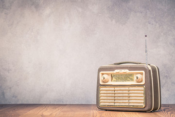 Retro portable broadcast radio receiver with leather case design from circa 1950s on wooden table front textured concrete wall background. Listen music concept. Vintage old style filtered photo