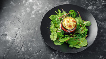 Baked Eggplant with tomato, mozzarella and green salad in a black plate