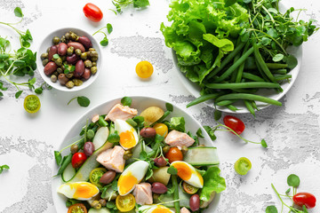 Healthy Nicoise salad with salmon, colourful sweet cherry tomatoes, olives, green beans, cucumber ribbons, soft boiled eggs, water-cress leaves with Mediterranean seasoning