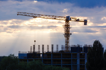 Industrial construction cranes and building silhouettes over sun at sunrise.