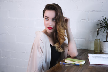 The girl sits at the table with a notebook and a book turned half-turned and looks over her shoulder.