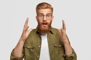 Amazed puzzled red haired male with astonished expression, gestures with hesitation and shock,...