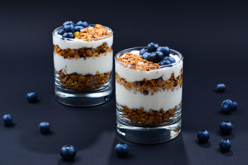 Homemade baked granola with yogurt and blueberries in a glass on a black background. Space for text or design.