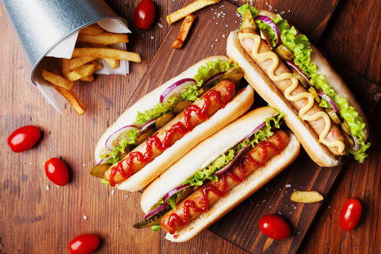 Hot Dog With Grilled Sausage, Ketchup, Mustard And Fries On Wooden Kitchen Board Top View. Traditional American Fast Food.