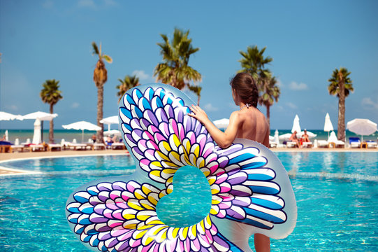Sexy woman holding inflated buttfly float in front of blue swimming pool
