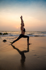 Middle age woman in black doing yoga on sand beach in India