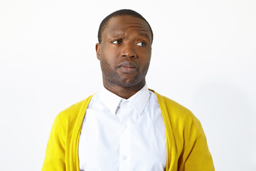 Picture of irritated unhappy young dark skinned man frowning and looking sideways with grumpy expression, annoyed with disturbing sound, posing isolated against white studio wall background