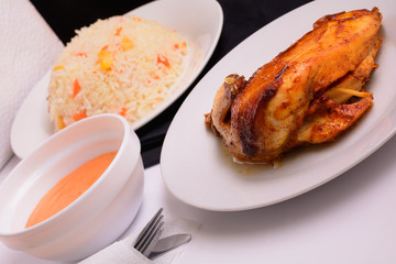 Grilled chicken on a white plate with sauce in a bowl and risotto flat lay