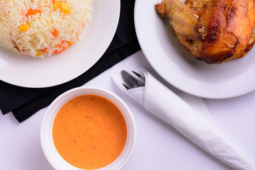 Grilled chicken on a white plate with sauce in a bowl and risotto flat lay