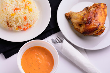 Grilled chicken on a white plate with sauce in a bowl and risotto flat lay