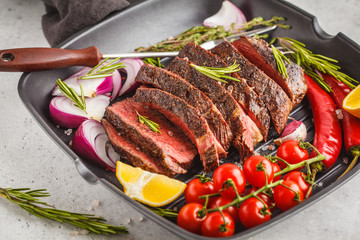 Sliced roast beef in a frying pan with spices and vegetables, white background, macro