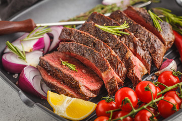 Sliced roast beef in a frying pan with spices and vegetables, white background, macro