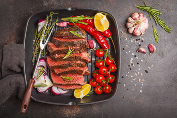 Sliced roast beef in a frying pan grill with spices and vegetables, top view, copy space.