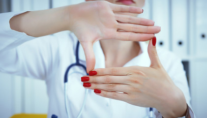 Young female doctor holding hands with advertising area between them and smiling on medical office in background. Photo with depth of field