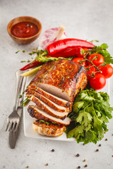 Roasted pork with thyme, rosemary, garlic and tomato sauce on a white dish, white background, vertical