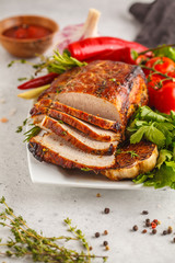 Roasted pork with thyme, rosemary, garlic and tomato sauce on a white dish, white background, vertical