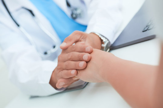 Hand of male doctor reassuring his female patient close-up. Medical ethics and trust concept.
