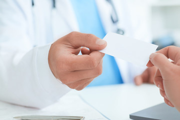 Male doctor's hand give white blank calling card to woman closeup in office. Physical, disease prevention, examine patient, instrument shop, healthy lifestyle, family doctor concept