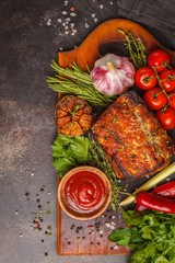 Baked pork with thyme, rosemary, garlic on a wooden board, dark background, top view, copy space.