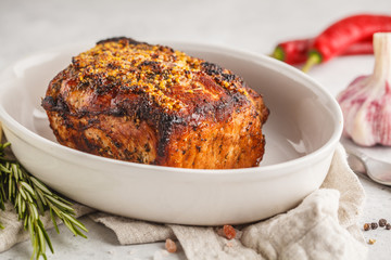 Whole piece of roast pork with mustard, rosemary, garlic in white dish, white background, copy space.