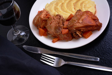 Cooked chicken under sauce with smashed potatoes and glass of wine on table with black table cloth