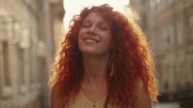 Sunshine young smiling woman with red curly hair look at camera smile walking in the city streets portrait happy slow motion summer face sunset beautiful lady outdoor closeup cute