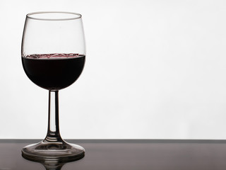 Close up of pouring of red dry wine in a crystal wine glass from full bottle of wine with splashes on a white isolated background
