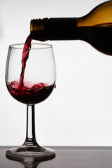 Close up of pouring of red dry wine in a crystal wine glass from full bottle of wine with splashes on a white isolated background