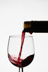 Close up of pouring of red dry wine in a crystal wine glass from full bottle of wine with splashes on a white isolated background