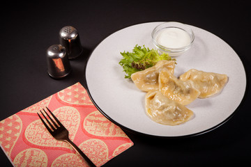 Vareniki, a traditional dish of Ukrainian, Polish and Russian cuisines - dumplings with various fillings, on a plate, on a black background.