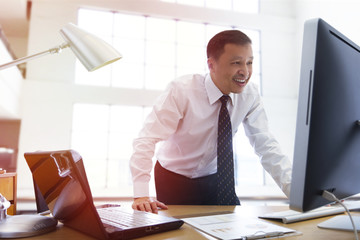 Fototapeta premium Asian businessman with smiley face standing and looking into a desktop computer in the office.