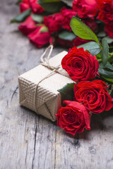 A gift box and bouquet of red roses on a wooden background. Gift set.